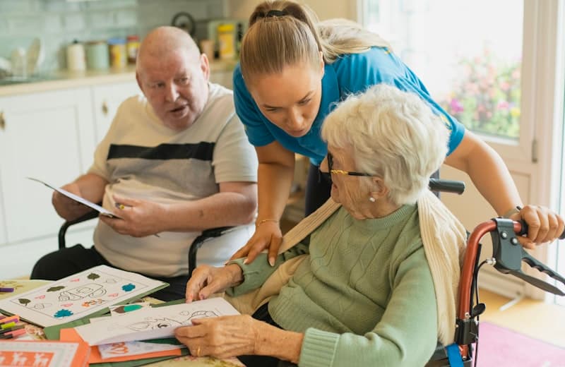 A home caregiver helping two seniors with an activity at home